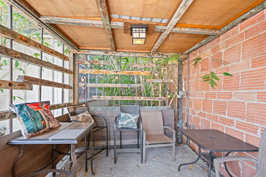 Cozy covered patio with rustic wood lattice and exposed brick, bistro tables and mixed chairs with patterned throw pillows, string lights and bamboo privacy greenery.