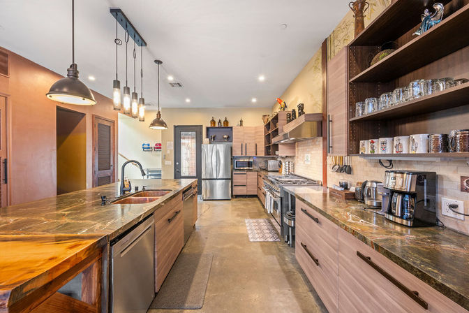 Spacious modern open-concept kitchen with a large stone island, pendant lights, stainless steel refrigerator and range, wood cabinets and open shelving
