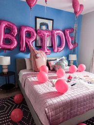 Bedroom party setup with metallic pink letter balloons on a blue wall, pink round balloons scattered across a pink-quilted bed with a disco-ball pillow and bedside lamps.