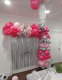 Cheerful pink and silver balloon arch with cow-print balloons and a star accent framing a silver fringe photo backdrop in an indoor party setting.