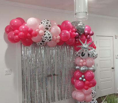 Cheerful pink and silver balloon arch with cow-print balloons and a star accent framing a silver fringe photo backdrop in an indoor party setting.