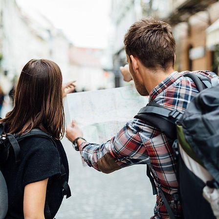 Two backpackers consulting a paper map and pointing on a cobblestone city street — urban sightseeing and travel