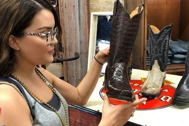 Customer inspecting a dark brown leather cowboy boot among patterned western boots on a retail display