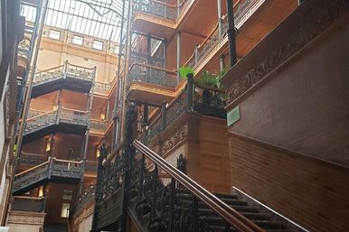 Grand historic atrium featuring ornate wrought-iron railings, a sweeping dark-wood staircase, stacked balconies and a soaring glass skylight overhead.