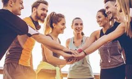 Group of young adults in athletic wear joining hands in an outdoor team workout huddle at sunset — energetic group fitness motivation.