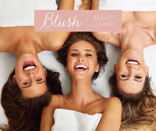Three smiling women in white towels lying head-to-head at a day spa, enjoying a beauty lounge pampering session