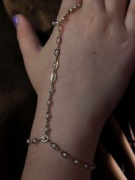 Close-up of a wrist wearing a delicate gold hand chain with small pearl beads against a dark background