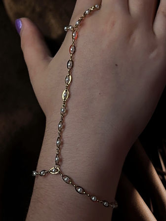 Close-up of a wrist wearing a delicate gold hand chain with small pearl beads against a dark background