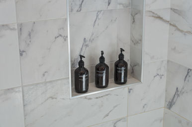 Marble-tiled shower niche with three amber pump bottles on a recessed shelf — minimalist bathroom soap and shampoo display