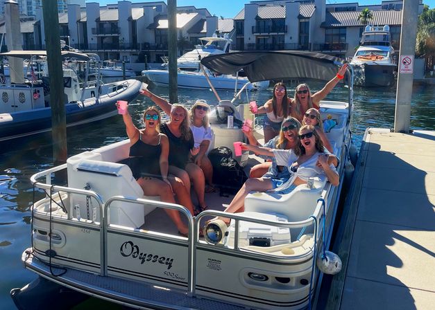 Group of friends cheering with pink cups on a pontoon boat docked at a sunny marina, yachts and waterfront condos in the background