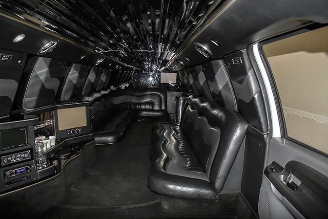 Spacious luxury stretch limousine interior with black leather bench seating, mirrored ceiling, ambient LED lighting, built-in bar and entertainment screens — party-ready limo cabin.