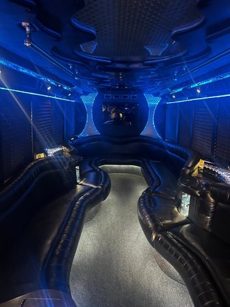 Party bus interior with curved black leather wraparound seating, central aisle, blue LED accent lighting, mirrored disco panels and built-in cup holders