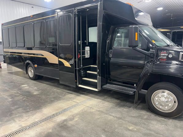 Sleek black commercial shuttle bus with gold accent stripe parked inside a garage, passenger door open revealing entry steps.