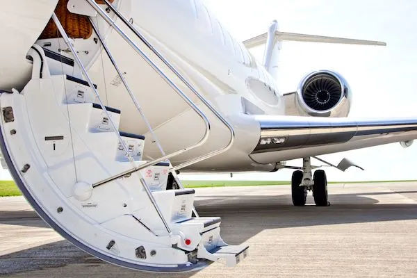 White private business jet on an airport tarmac with folding boarding stairs extended, rear turbine engine and tail visible on a sunny day
