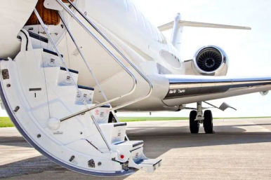 White private business jet on an airport tarmac with folding boarding stairs extended, rear turbine engine and tail visible on a sunny day