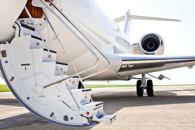 White private business jet on an airport tarmac with folding boarding stairs extended, rear turbine engine and tail visible on a sunny day