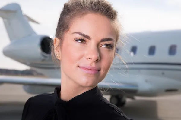 Confident woman with a subtle smile standing on an airport tarmac in front of a private jet — business travel portrait