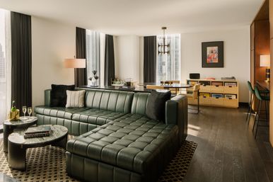 Modern downtown high-rise living room with dark green tufted leather sectional, marble coffee tables, dining nook and floor-to-ceiling city-view windows