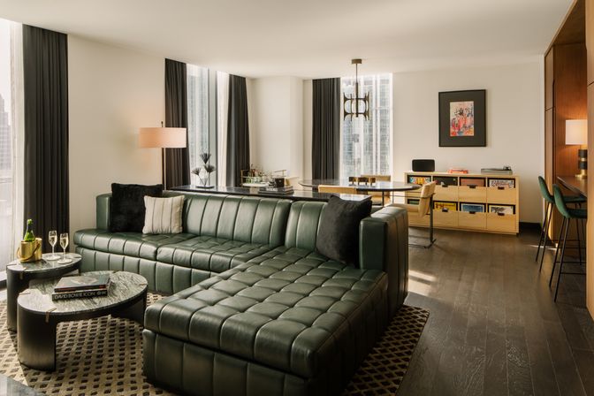 Modern downtown high-rise living room with dark green tufted leather sectional, marble coffee tables, dining nook and floor-to-ceiling city-view windows