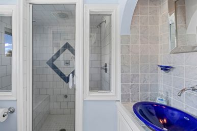 Glass-enclosed white-tile shower with blue diamond tile accent and bench, adjacent to marble mosaic wall and glossy cobalt-blue vessel sink with chrome faucet.