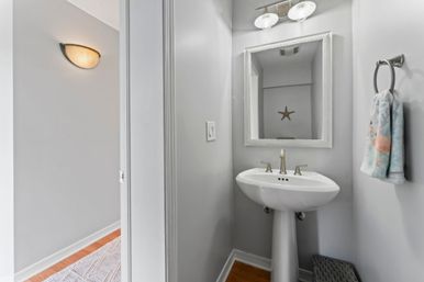 Small modern powder room with white pedestal sink, chrome faucet, framed mirror, gray walls and coastal accents (starfish wall art and flamingo towel)