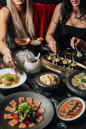 Two diners enjoying sushi and sashimi bites with cocktails and smoky dry-ice presentation on a marble table in an upscale city restaurant.