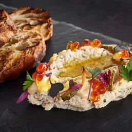Gourmet seafood rillettes topped with fish roe, cornichons, microgreens and olive oil on a slate plate, served with grilled sourdough crostini.