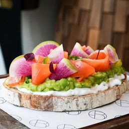 Vibrant brunch avocado toast on rustic sourdough with whipped ricotta, mashed avocado, smoked salmon rosettes, thin watermelon radish slices and microgreens