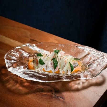 Citrus-marinated gourmet seafood salad with thin white shreds and mint leaves on a textured glass platter atop a wooden table
