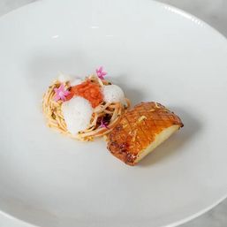Fine-dining plate with a small nest of seafood pasta topped with foam, salmon roe and pink edible flowers, paired with a glazed, scored seared scallop on a white plate