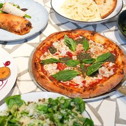 Mouthwatering Italian-style pizza topped with pesto, fresh basil and roasted peppers, served with pasta, green salad and appetizers on a patterned table