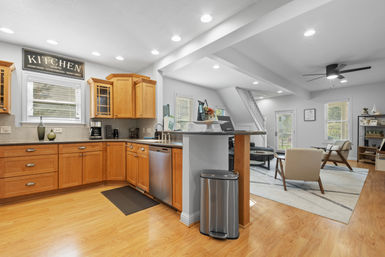 Cozy open-concept kitchen and living area with warm wood cabinets, stainless dishwasher, breakfast bar island, hardwood floors, recessed ceiling lights and modern ceiling fan.
