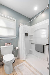 Bright modern gray-and-white residential bathroom with walk-in shower, curved shower rod, grab bars, towel and toilet