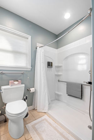 Bright modern gray-and-white residential bathroom with walk-in shower, curved shower rod, grab bars, towel and toilet
