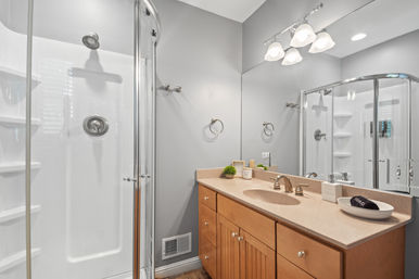 Contemporary gray bathroom with curved glass corner shower, wood vanity countertop, brass faucet and illuminated mirror