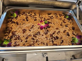 Hearty seasoned rice and red beans in a stainless-steel buffet chafing dish, garnished with bright purple orchid flowers