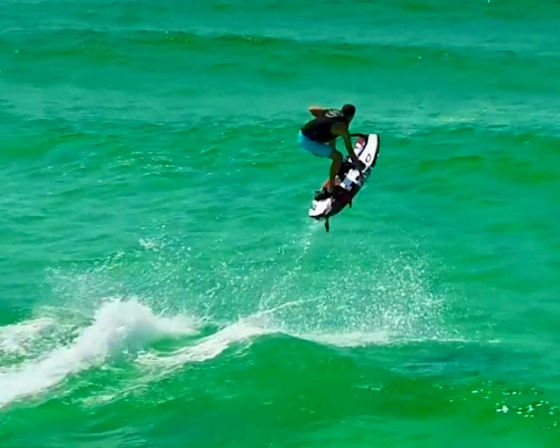 High-flying jet ski rider jumping over turquoise ocean waves, water spray and wake trailing behind in an action-packed water sports scene.