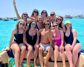 Smiling group of friends in swimsuits on a boat in clear turquoise water on a sunny summer bachelorette-style boat party.