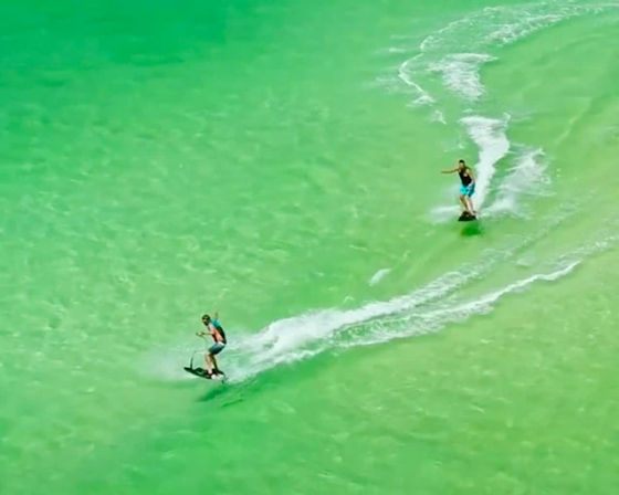 Aerial shot of two wakeboarders carving curvy white wake trails across bright emerald-green tropical water