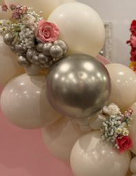 Elegant blush and metallic silver balloon garland adorned with pink and white faux roses and baby's breath on a pink event backdrop