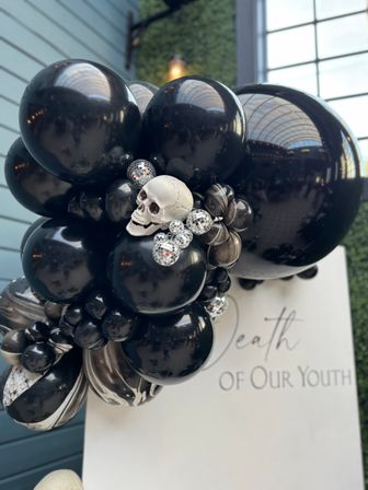 Glossy black and marbled balloon garland with a decorative skull and mirrored disco ball accents, styled as a spooky-chic indoor event backdrop.