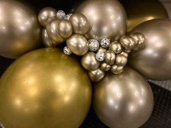 Close-up of clustered metallic gold and champagne balloons accented with small mirrored disco-ball ornaments, festive indoor party decor
