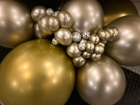 Close-up of clustered metallic gold and champagne balloons accented with small mirrored disco-ball ornaments, festive indoor party decor