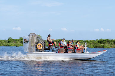 Airboat skimming marsh waters in the Florida Everglades with a guide at the rear and passengers wearing ear protection on a wetland tour