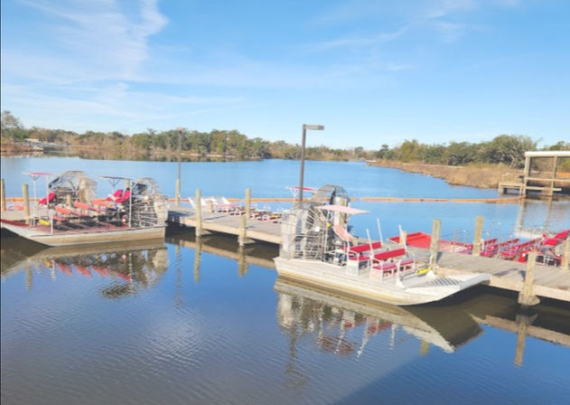 Bright red-seated airboats lined at a wooden dock on a glassy river, reflecting clear blue sky and marshy shoreline