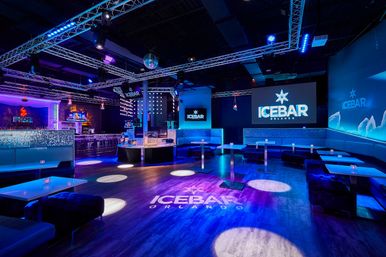 Vibrant blue-purple ice-themed lounge interior in Orlando with illuminated bar, booth seating, high tables, disco ball, and projected snowflake logo.