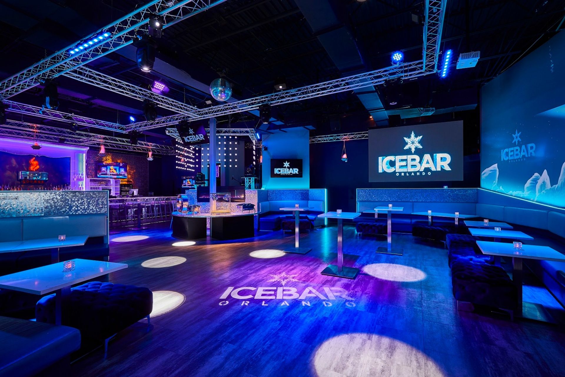 Vibrant blue-purple ice-themed lounge interior in Orlando with illuminated bar, booth seating, high tables, disco ball, and projected snowflake logo.