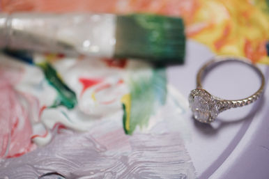 Close-up of a sparkling diamond ring resting on pastel floral fabric with a soft, colorful background blur