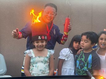 Backyard kids' party: a costumed performer lights a tall novelty hat that bursts into bright flames atop a smiling girl’s head while other children watch nearby.