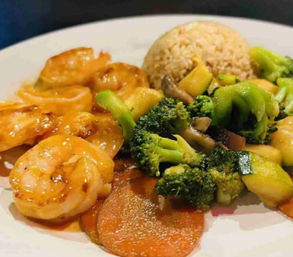 Close-up of shrimp stir-fry: glazed shrimp with broccoli, zucchini, carrots and mushrooms served with a scoop of brown rice on a white plate.